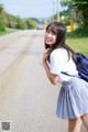 A young woman in a school uniform standing on the side of a road.